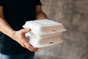 A man holds two white takeout boxes of food.