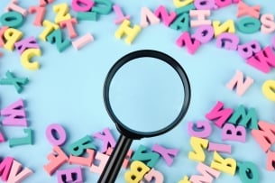 A magnifying glass hovers over scattered letters on a blue background.