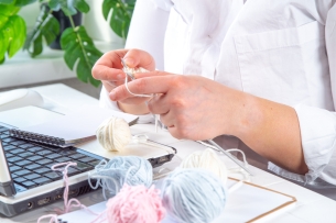 hands knitting over a computer with a ball of yarn to one side