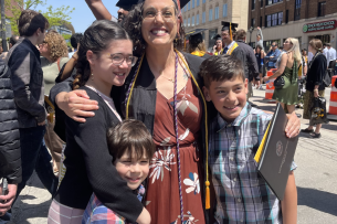 Student Rachel Goochey smiles in her graduation regalia, hugged by her three children.