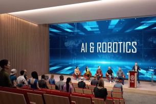 A computer-generated image of a lecture hall filled with people looking at a screen that shows the text "AI and Robotics"